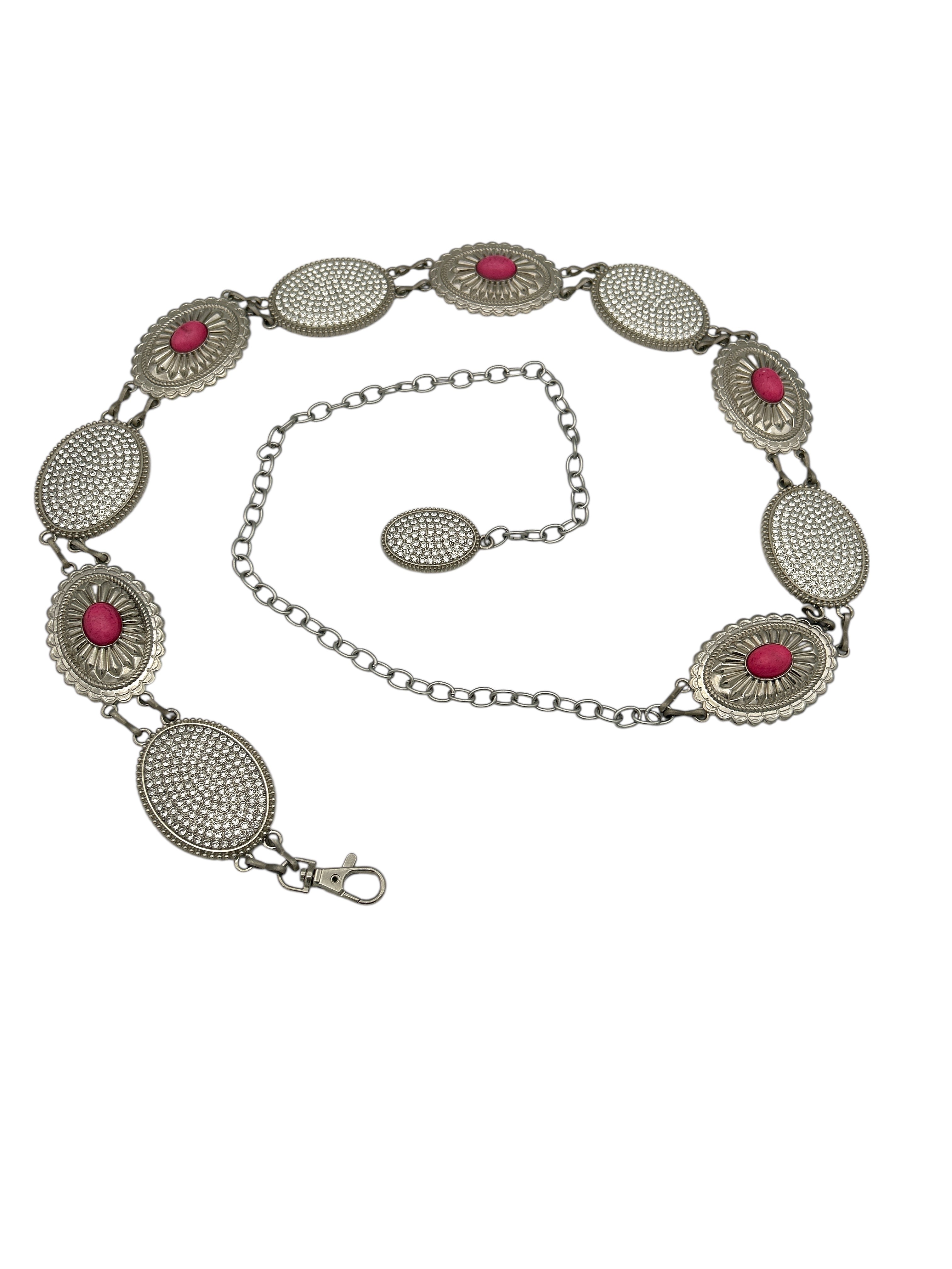 Silver Western metal concho belt with oval, intricately engraved conchos, some featuring pink centers and others studded with rhinestones.
