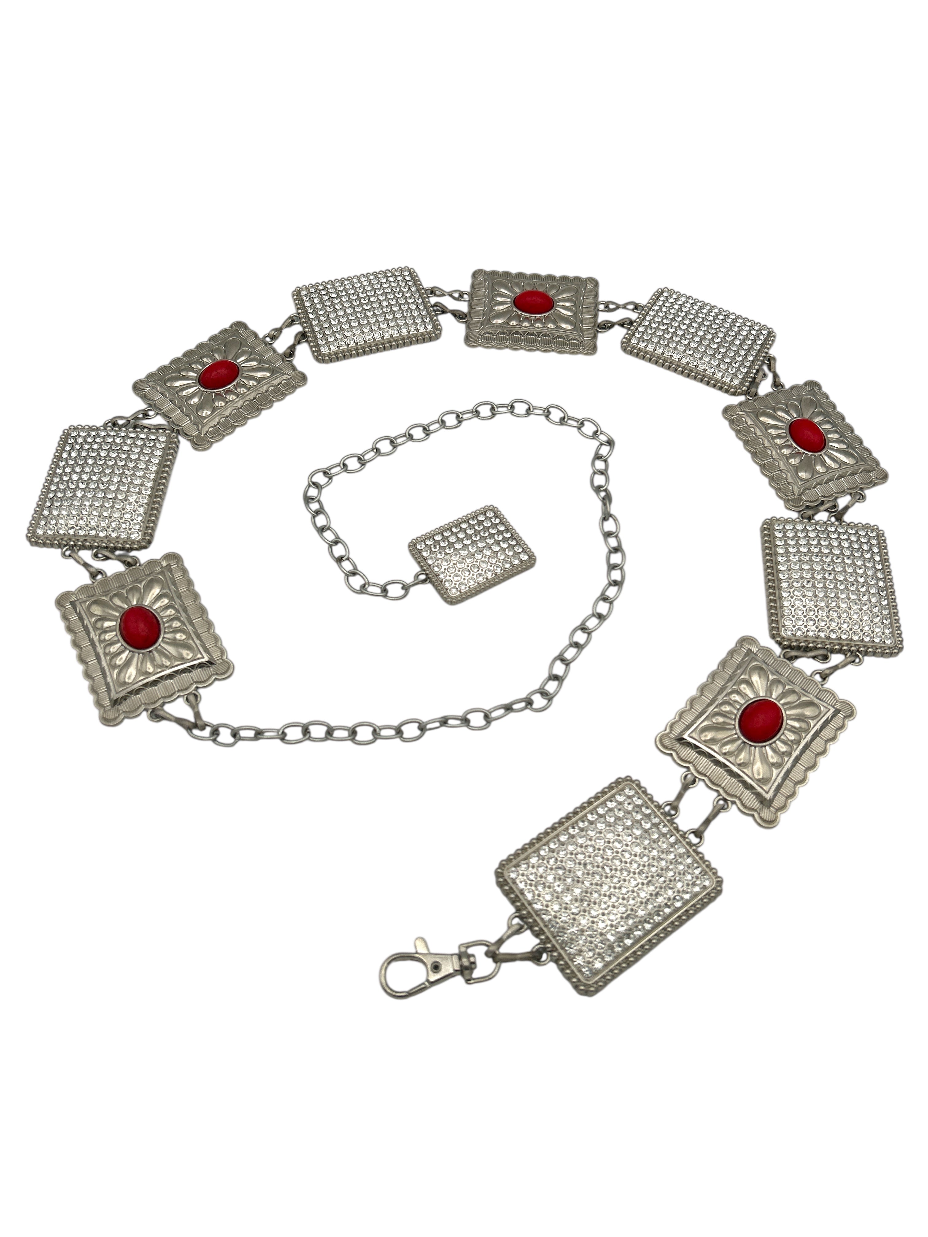 Silver Western metal concho belt with square, intricately engraved conchos, some featuring red stones and others covered in clear rhinestones.