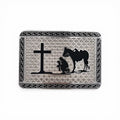 Silver tone buckle with black silhouette of a kneeling cowboy, horse, and cross, framed by a geometric border.