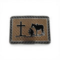 Two-tone gold and silver buckle with black silhouette of kneeling cowboy, horse, and cross, geometric border.